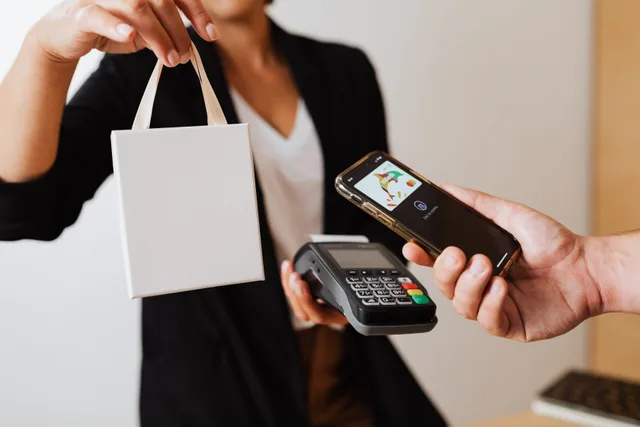 A person uses a smartphone for contactless payment with a payment terminal, while receiving a shopping bag. Common omnichannel marketing questions about continuity