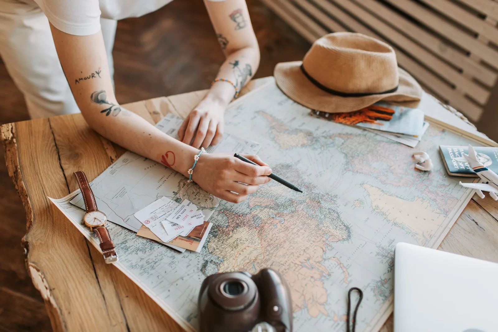 Tattooed woman planning a trip with a world map, passports, and travel essentials on a wooden table. How to use digital customer journeys benchmarks in planning