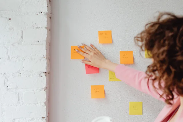 A woman planning ideas with colorful sticky notes on a wall. Ideal for conceptual and organizational themes. Digital customer journeys checklist: the items people skip
